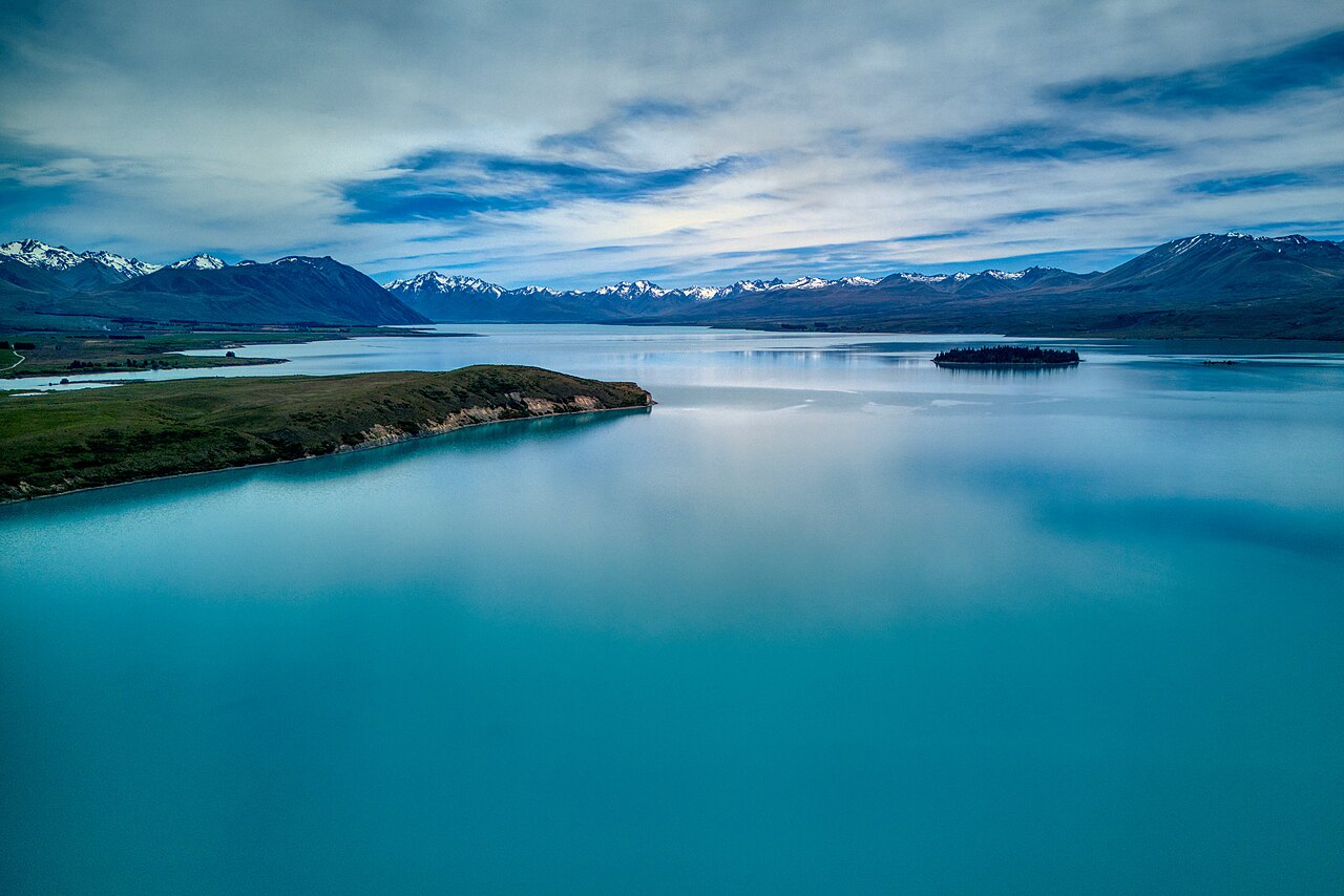 Lake Tekapo turquoise blue waters with lupin flowers in bloom along the stony shore